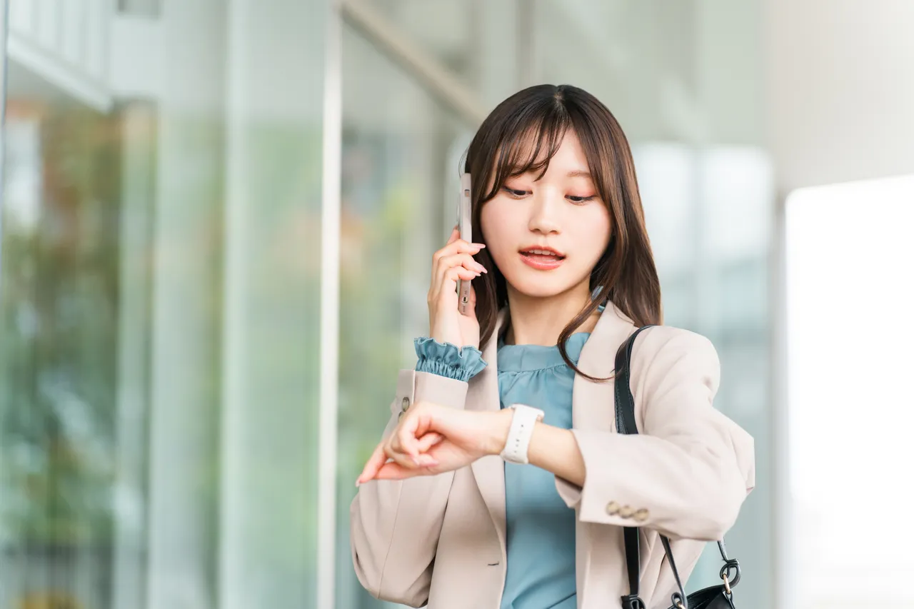 腕時計を見ながらスマートフォンで電話をかける女性