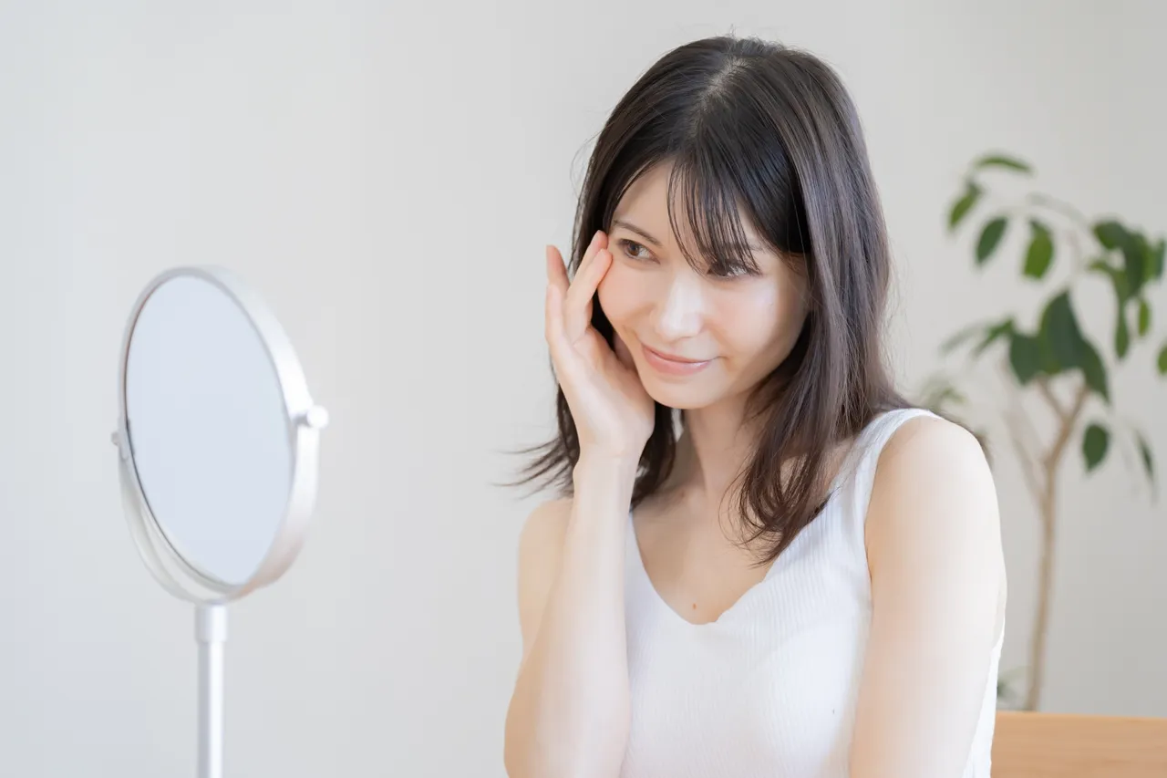 鏡の前で肌を確かめてほほえむ女性