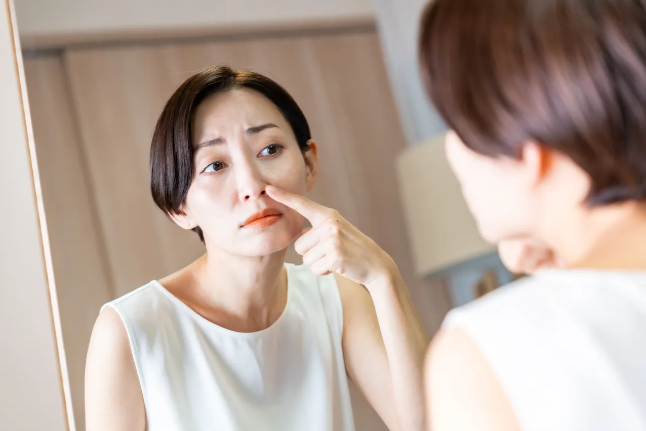 鏡を見ながら小鼻に触れる女性