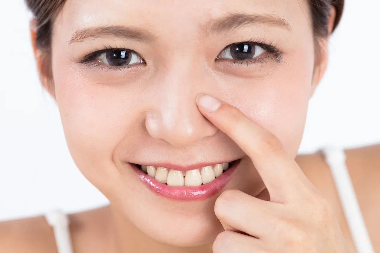 笑顔で小鼻に指を添える女性