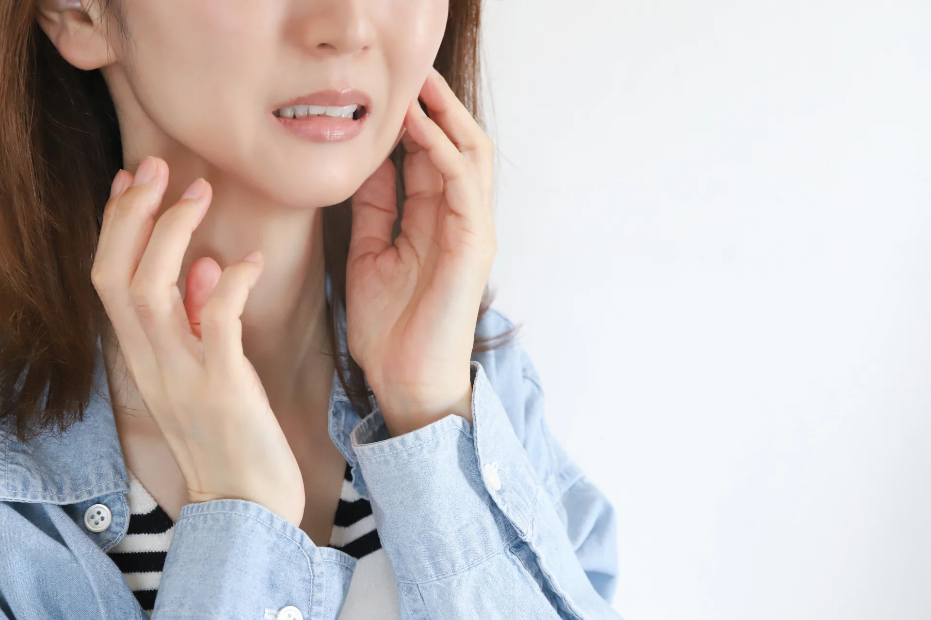 顔をしかめて両手であごのつけ根に触れる女性（噛みにくさなど施術後の違和感のイメージ）