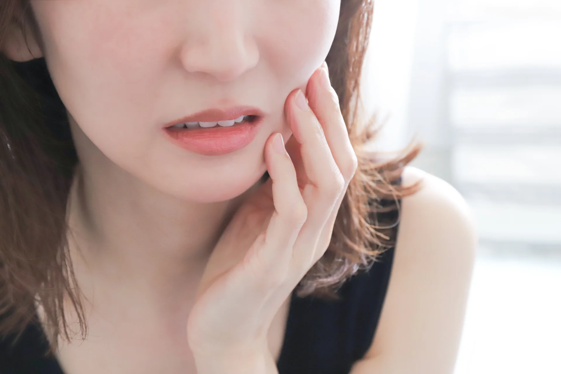 頬に手を当て、痛みをこらえるように口元をゆがめる女性。術後の腫れや痛みのイメージ