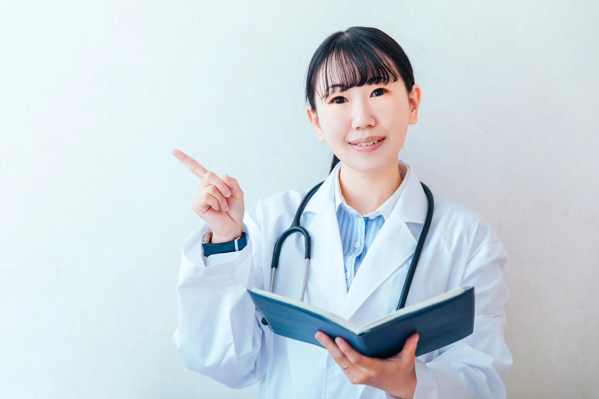 ノートを持ち指をさして説明する白衣の女性医師(よくある質問への回答のイメージ)