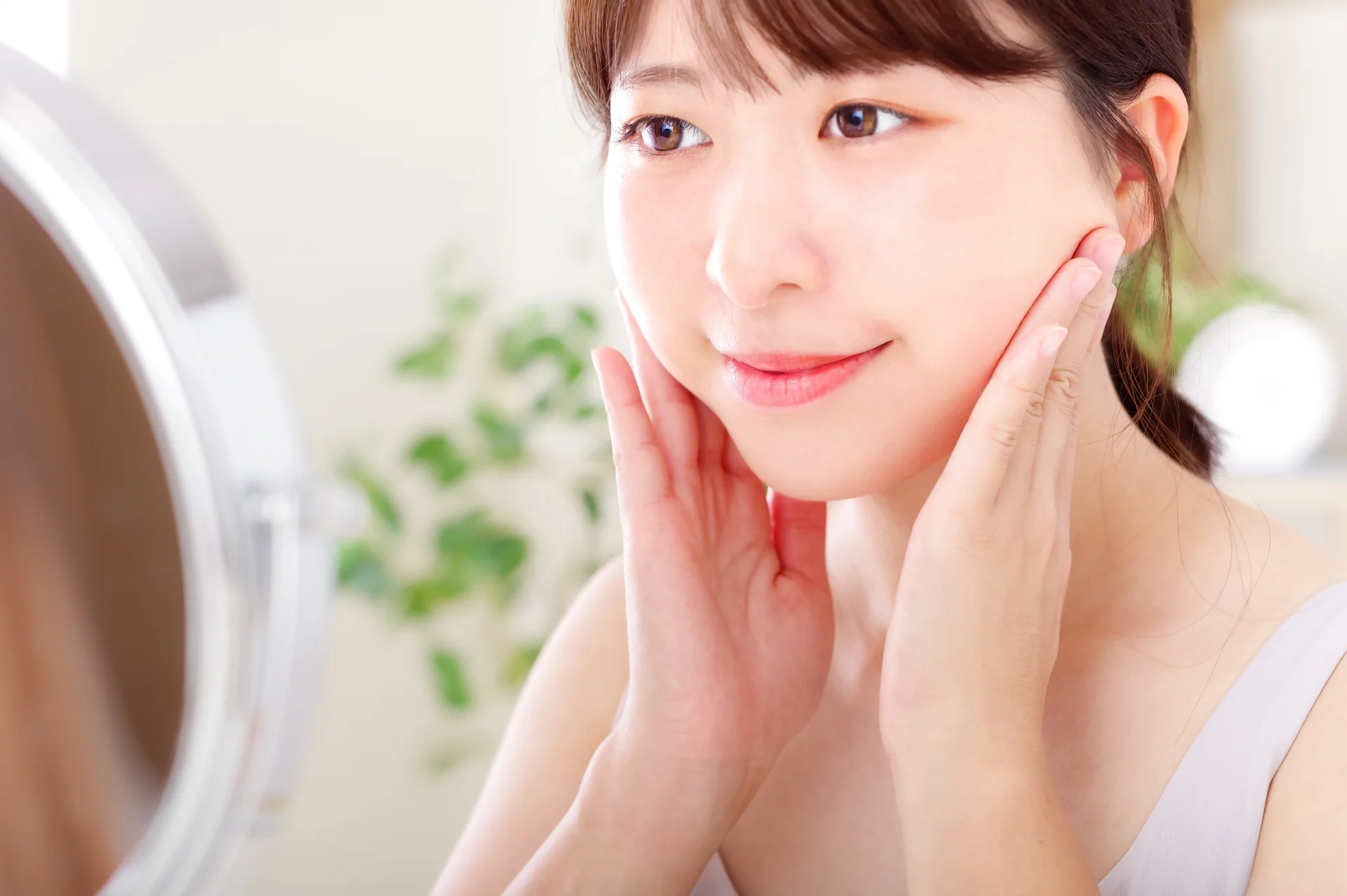 鏡の前で両手を頬に添えてほほえむ女性