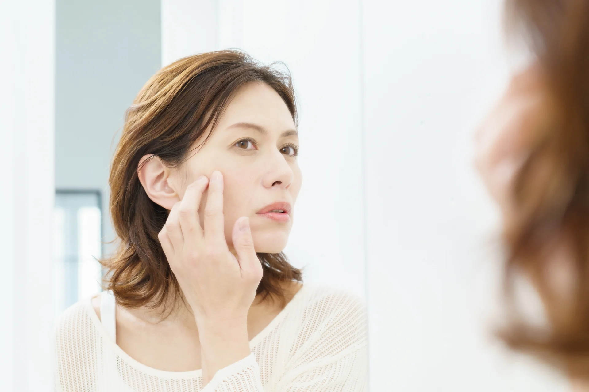 鏡の前で頬に指を当てて肌の状態を気にする女性