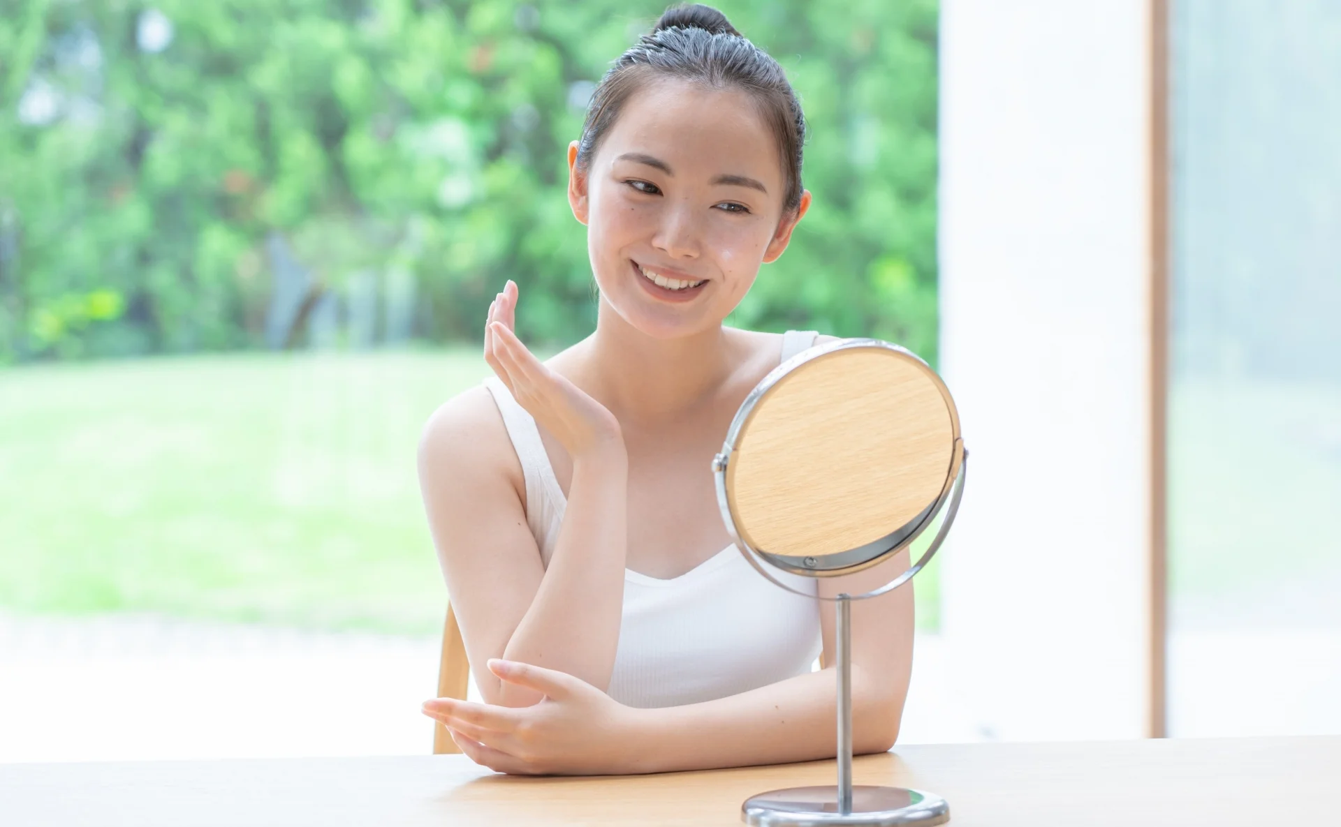 卓上ミラーの前で頬のそばに手を添えてほほえむ女性