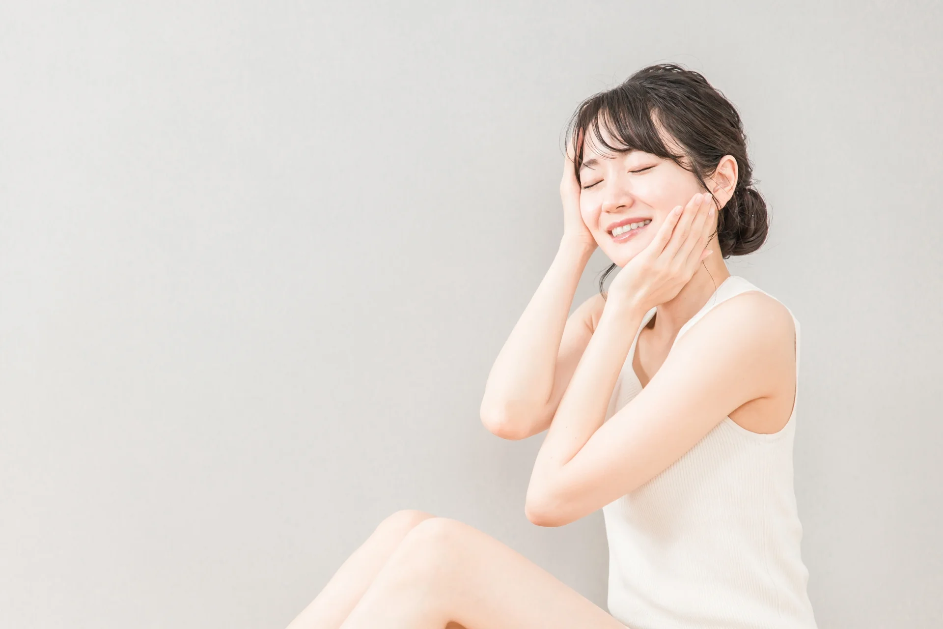 両手を頭と頬に添え、目を閉じて笑顔を見せる女性（悩みの原因から頬の整形を選ぶまとめのイメージ）