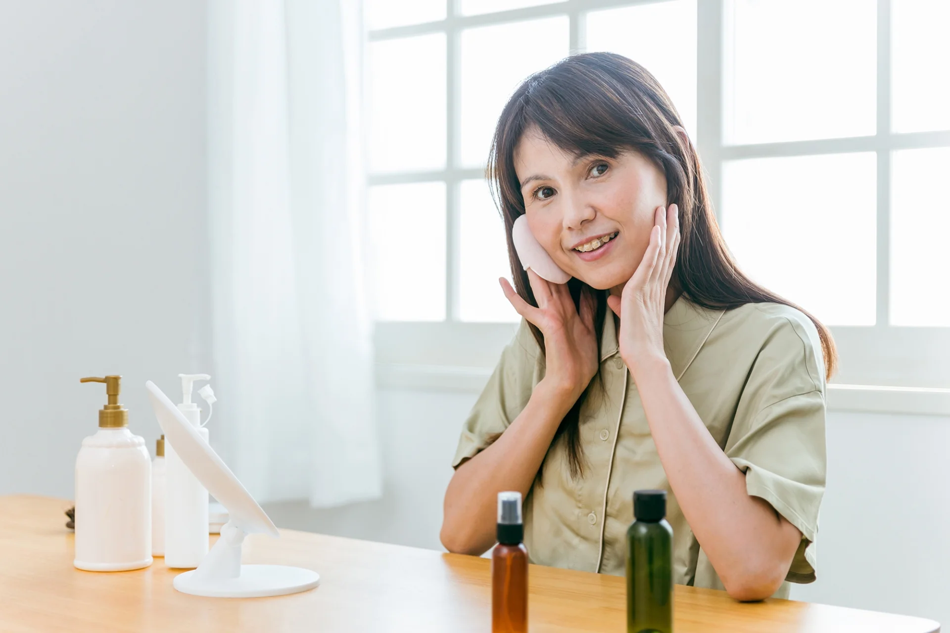 鏡の前で両手を頬に当て、頬の感触を確かめる女性