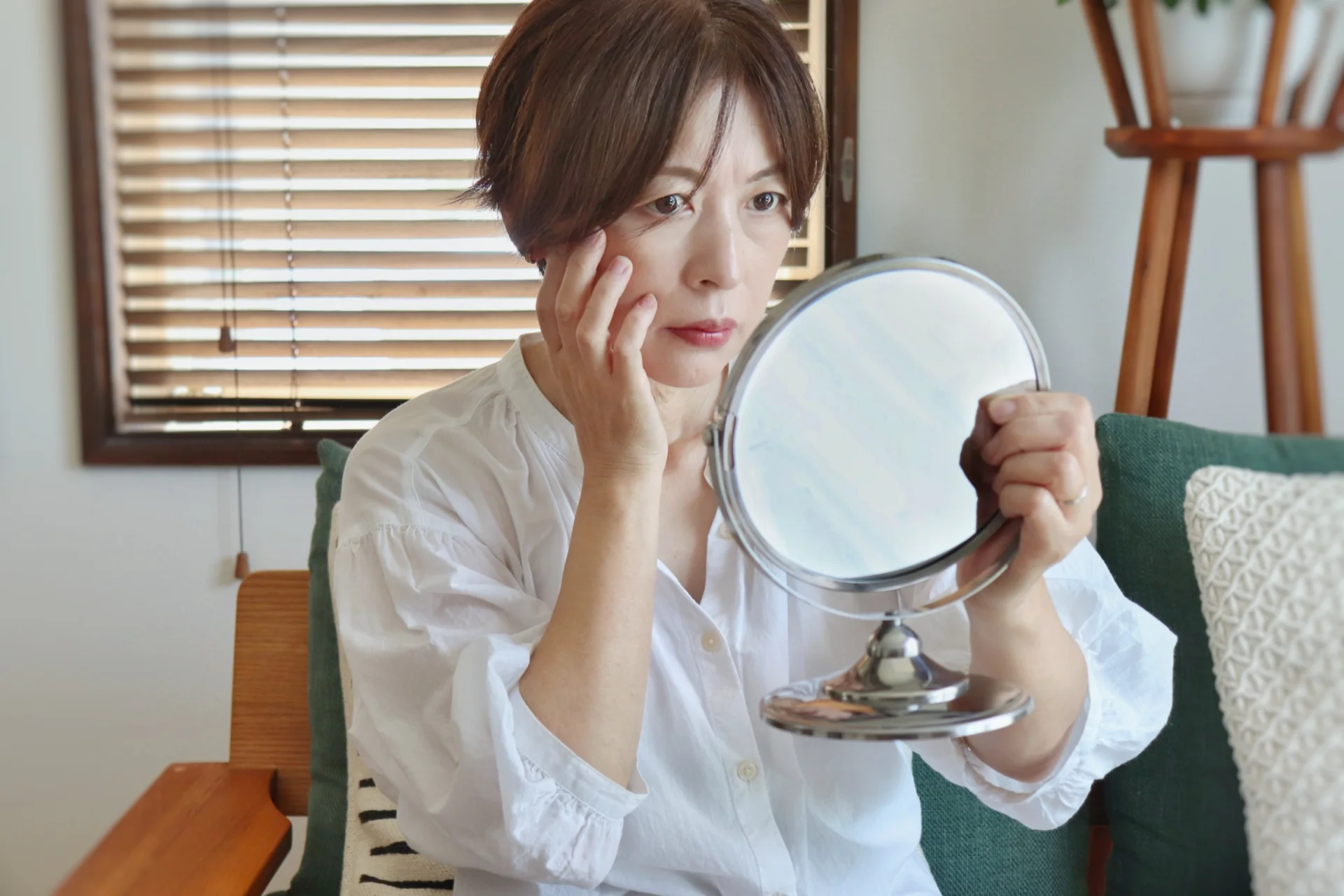 手鏡を持って目元から頬に指を当てる女性(頬の肉の疑問を確かめるイメージ)