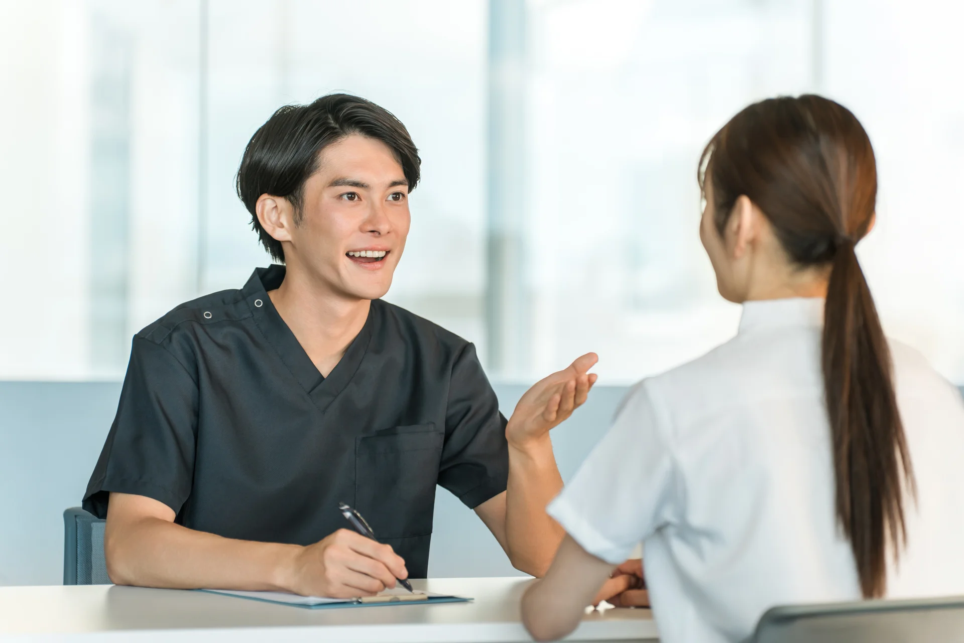 スクラブ姿の医療スタッフが記録をとりながら女性の相談を聞く場面（原因に合う相談先で話を聞いてもらうイメージ）