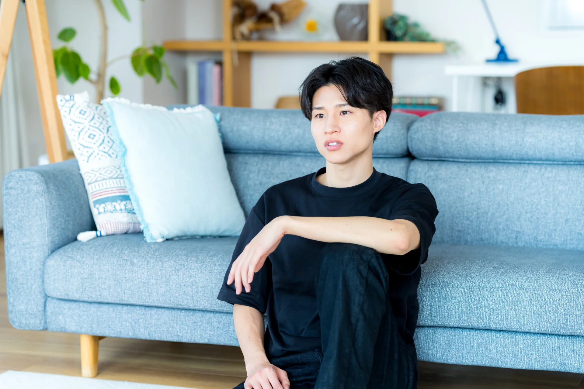 ソファの前に座る若い男性（若い人や男性にも起こる頬こけのイメージ）