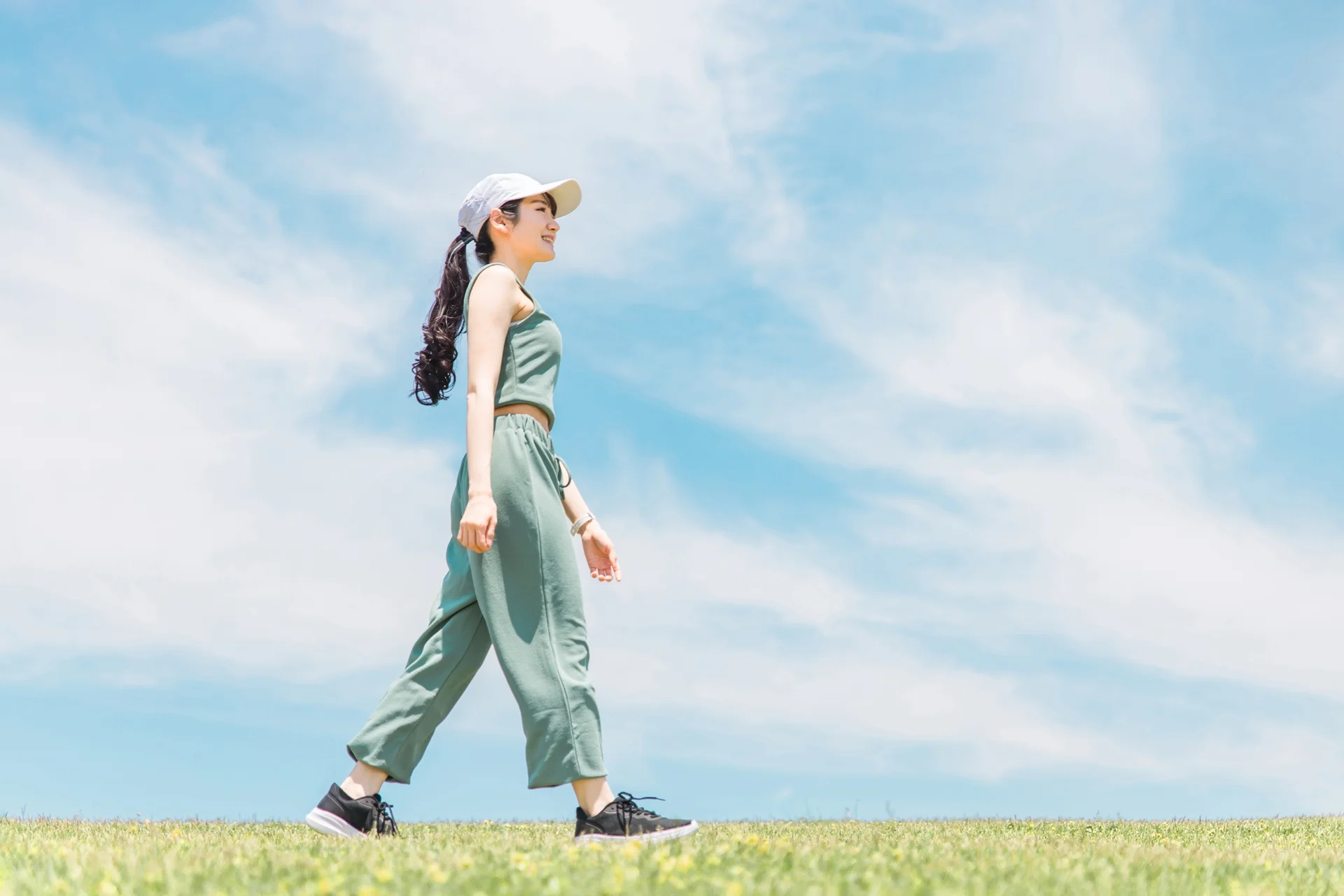 青空の下の草地をウォーキングする女性